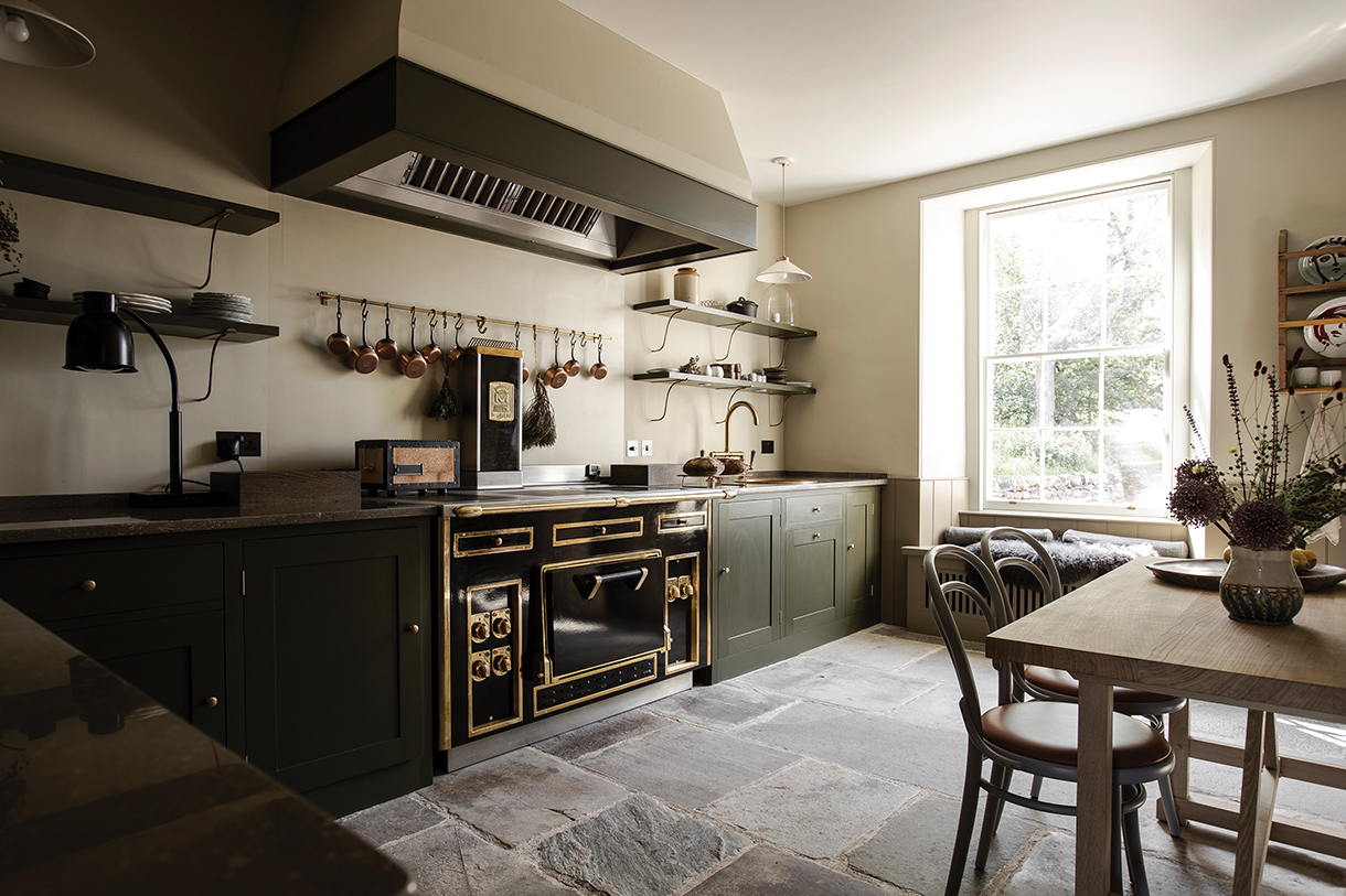 Refined farmhouse kitchen with Old World aesthetics, classical black enamel range, exposed shelving, stone floors.